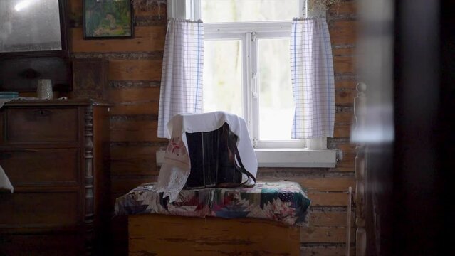 An old accordion in Russian style stands on the windowsill in a wooden ancient house covered with a white embroidered napkin in the afternoon in winter, will play the melody of folk songs. Close-up