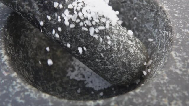 Close-up of a white sea salt falling on the pestle in the grey stone mortar