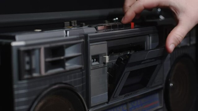A man's hand inserts a cassette into a tape recorder and presses the play button