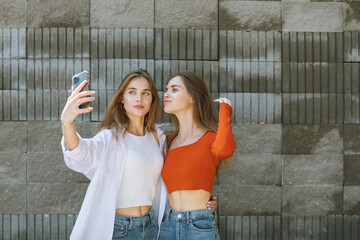 Portrait of twin sisters taking selfies on the street with a cellphone.