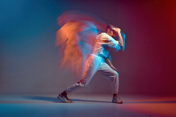 Sportive girl with short hair dancing hip-hop in stylish sportswear in colorful neon light at dance hall. Long exposure