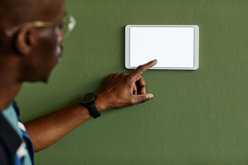 Minimal close up of African American man using smart home control panel with blank screen on green...