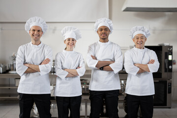 Portrait of a young multiracial group of cooks standing together in uniforms in the restaurant kitchen. Confident chefs ready for cook at restaurant. Team of European, Asian and Latin professionals - Powered by Adobe