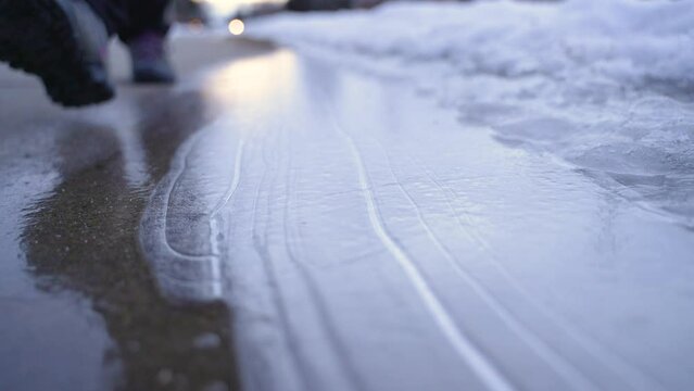 Woman's boot walking in slow motion, cracking ice on sidewalk. Closeup.