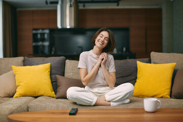 Obraz premium Touched smiling young girl feel happy from tender moment of romantic movie, sitting on comfortable couch at home