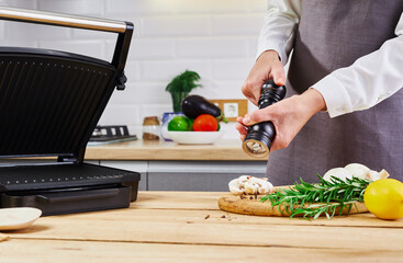 A woman using a pepper grinder to cook mushrooms.Fresh mushrooms, rosemary and lemon on a wooden board.