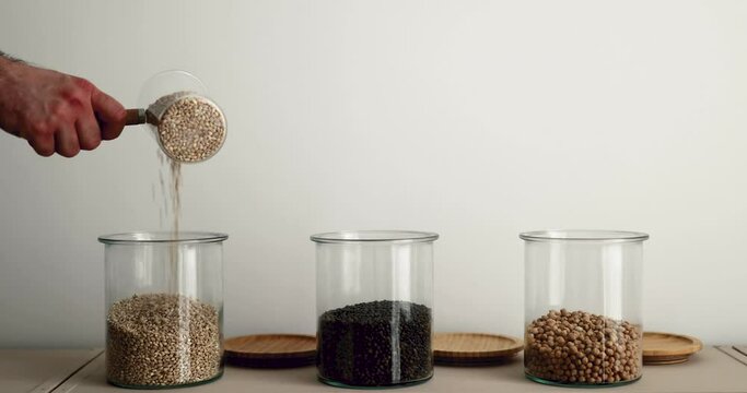 Refilling glass jars with pearl barley, lentils and chickpea. Pouring dried food from a small pot. Prepping idea for pantry food storage. Preparing for food shortage.  Zero waste idea.