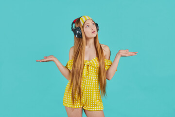 Young woman listening to music in headphones.Girl wearing yellow dress posing with arms outstretched and presenting something.