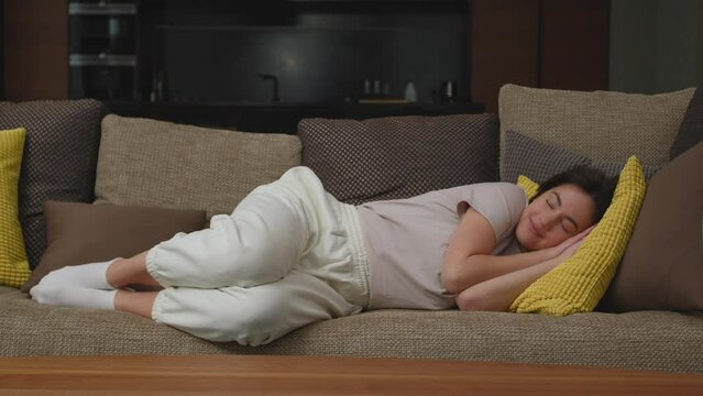 Serene happy woman lying sleeping on soft couch in living room, enjoy lazy free day. No stress, healthy sleep