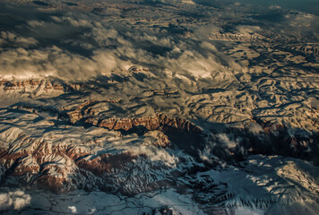 Aerial view from the plane of hills snow and mountains landscape with shadows of sunlight and clouds covered beautifully. Above the clouds, Snow capped mountain, No focus, specifically.