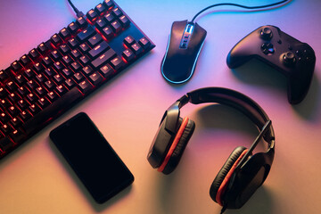 Gamer work space concept. gaming set up. top view of a gaming gear, keyboard, mouse, gamepad, joystick, headset and a smartphone on a colorful desk - obrazy, fototapety, plakaty