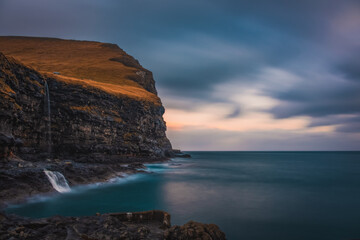 Rocky shore on a cloudy day. Cliffs of Kalsoy island. Early morning in Mikladalur, wild Faroe Islands. November 2021. Long exposure picture