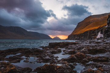 Fototapeta na wymiar Rocky shore on a cloudy day. Cliffs of Kalsoy island. Early morning in Mikladalur, wild Faroe Islands. November 2021