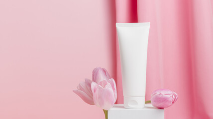 Fototapeta na wymiar Mockup unbranded tube of face cream on podium with tulips flowers, spring skin care concept, natural cosmetics, template tube for design and branding