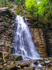Maniava waterfall. Vertical panorama. Waterfall in the Carpathian Mountains in the gorge. Cascades of water fall on shiny wet stones. Carpathian Mountains, Ivano-Frankivska oblast, Ukraine.