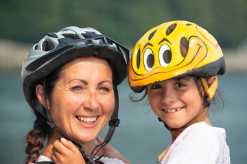 Portrait of a smiling woman with her daughter, wearing helmets and ready for riding bicycles, embracing each other.