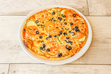 Mediterranean pizza with sliced black olives, tomato and zucchini with mozzarella cheese on a white plate