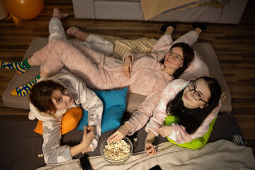 Female Friends Having Fun Together At Home Party. Yonung woman in funny onesies at pajama party.