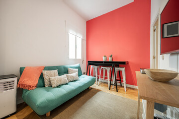 living room of a short-term rental apartment with a green sofa bed, a red painted wall and an oak wood sideboard and a black table