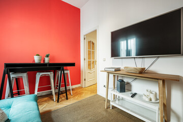  green sofa bed, a red painted wall and an oak wood sideboard with a large television above it and a natural fiber rug