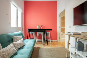 Fototapeta premium living room of a short term rental apartment with a green sofa bed, a red painted wall and an oak wood sideboard with a large television above it and a natural fiber rug