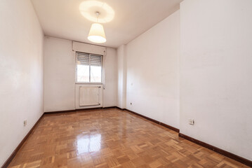 Empty living room with wooden parquet flooring with an aluminum radiator under the window