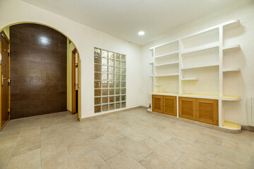 Empty living room with plaster bookcase and low wooden furniture and a wall of glass paves next to a semicircular arch