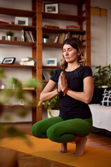 A middle-aged woman prays and practices yoga at home.