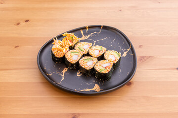 Thick maki dish stuffed with avocado, red rice and surimi on a pine wood table