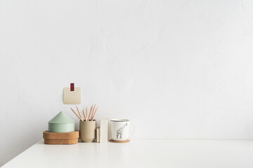 Front view white desk with supplies, mug and white wall copy space.	
