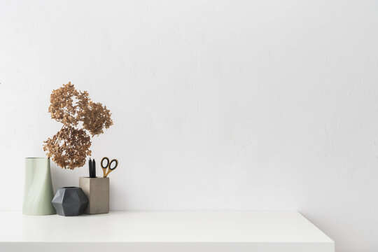 White desk with minimal vase with a decorative dried branches, flower against white wall.	

