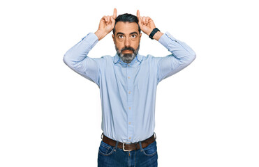 Middle aged man with beard wearing business shirt doing funny gesture with finger over head as bull horns