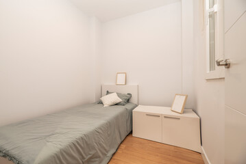 Fototapeta na wymiar Bedroom with single bed with gray bedspread, cushions, frames and white cabinets