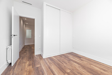 bedroom with wooden floors and white baseboards, doors and fitted wardrobes with sliding doors and...