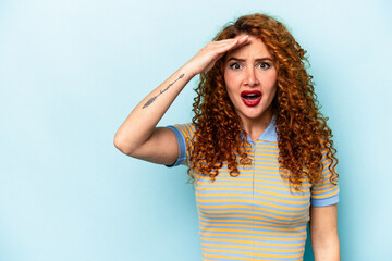 Young ginger caucasian woman isolated on blue background shouts loud, keeps eyes opened and hands tense.