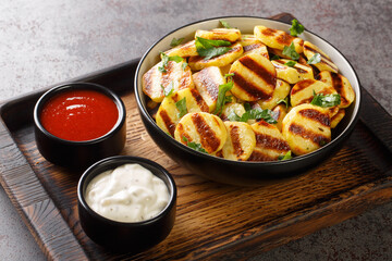 Hot sliced grilled baby potatoes with stripes and two sauces close-up on a wooden board on the...