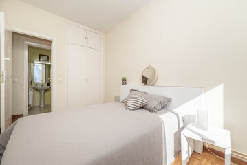 bedroom with king size bed with gray bedspread and cushions, white headboard, white wooden doors built-in wardrobe and en-suite toilet