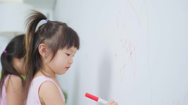 Asian young sibling kid girl enjoy paint on white wall in living room.	