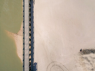 Bord de mer avec une personne dans le sable photographié en drone à côté d'un ponton et de l'océan. 