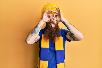 Redhead man with long beard football hooligan cheering game wearing funny wig doing ok gesture like...