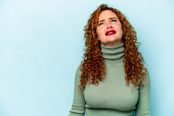 Young ginger caucasian woman isolated on blue background shouting very angry, rage concept, frustrated.