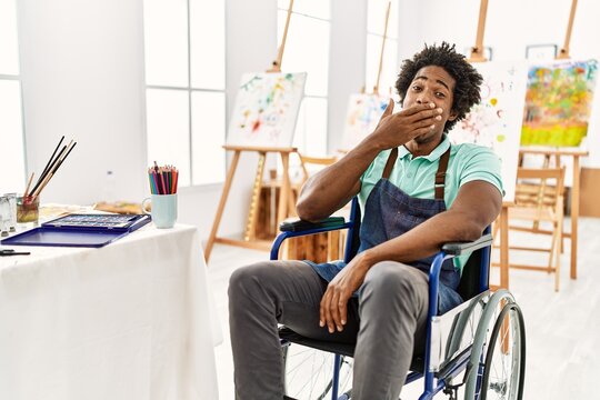 Young african american artist man sitting on wheelchair at art studio bored yawning tired covering mouth with hand. restless and sleepiness.