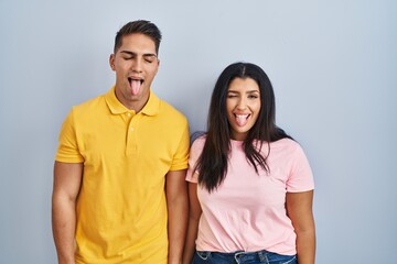 Fototapeta premium Young couple standing over isolated background sticking tongue out happy with funny expression. emotion concept.