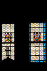 The Catholic cross at the top of the confessional against the background of a sunlit stained glass window. The photo was taken inside the church.