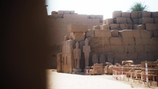 Tourist path outside the Karnak Temple in Luxor, Egypt. Large rocks and tall statues with fences around.
Sideways slide from behind a wall, low depth of field.