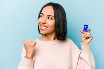 Young hispanic woman holding batteries isolated on blue background points with thumb finger away, laughing and carefree.