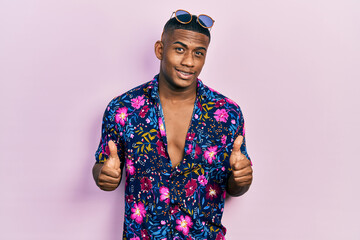 Young black man wearing hawaiian shirt and sunglasses success sign doing positive gesture with...