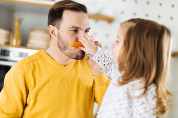 Father and his small daughter having fun with carrot in the kitchen