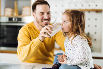 Cute girl drinking milk with her father in the kitchen. Focus is on girl