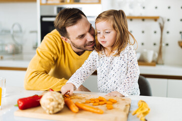 Single father and his small daughter preparing a meal in the kitchen. Focus is on girl